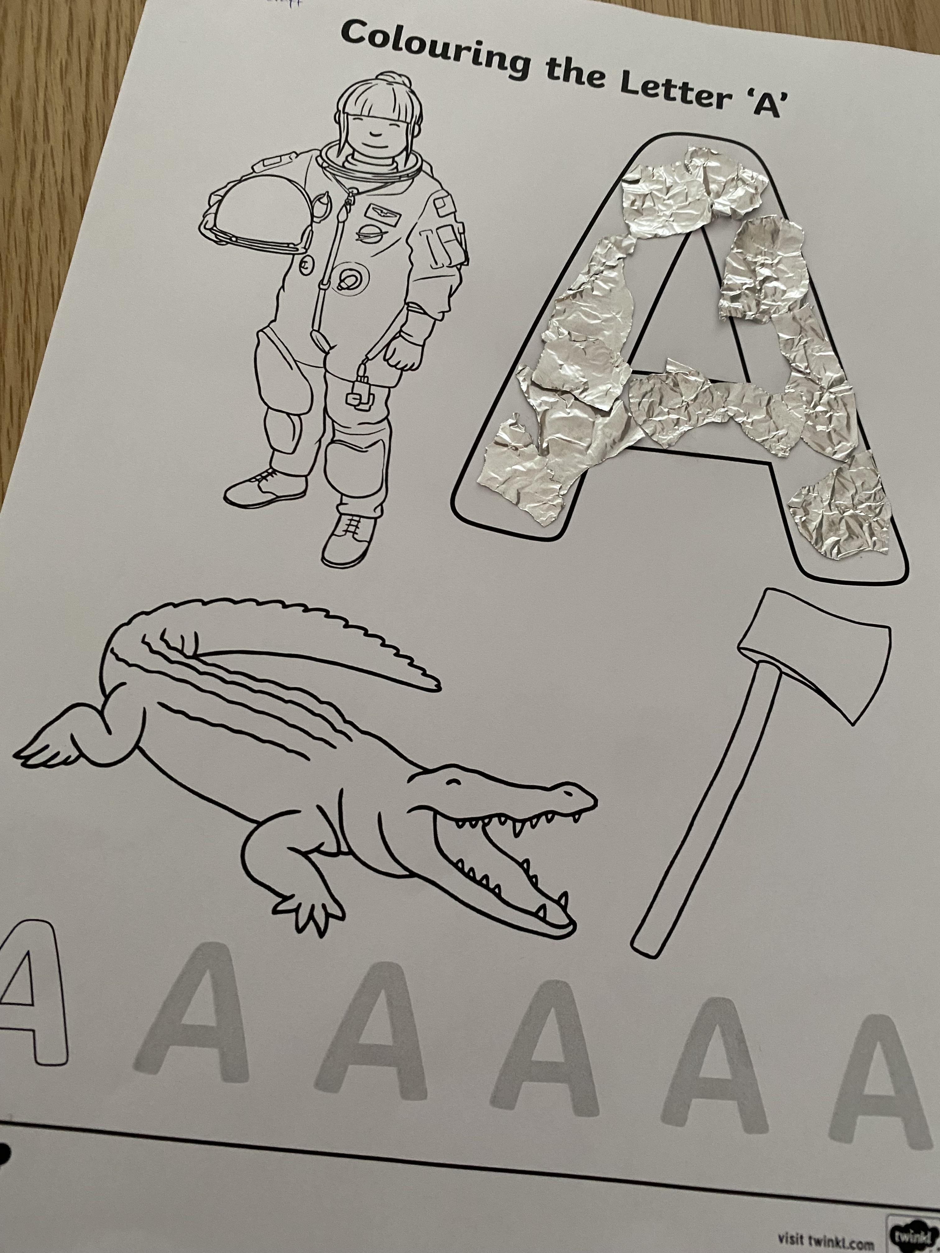 A children's colouring page with the letter A, with pictures of an astronaut, alligator and an axe